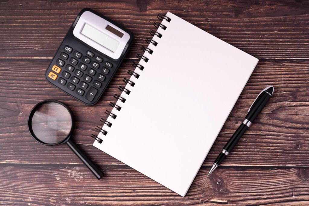 business valuation - Calculator blank notepad magnifying glass and pen on wood background